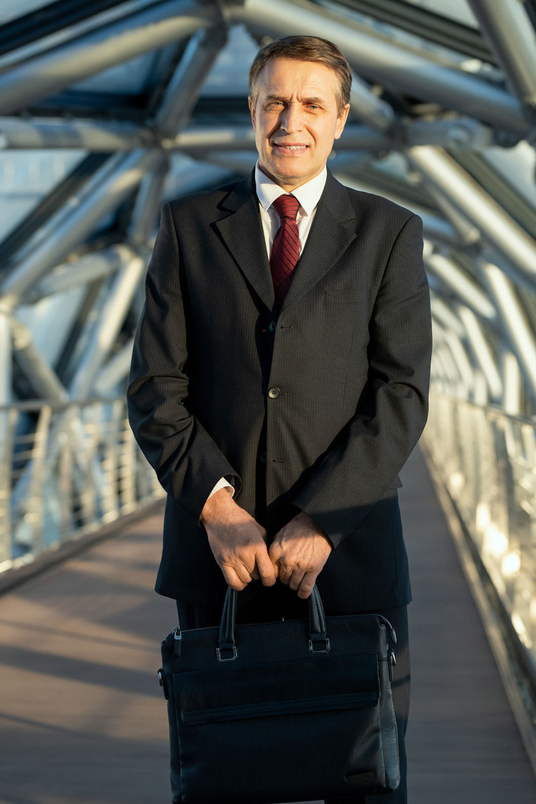 Mature elegant delegate or businessman with black leather handbag standing in front of camera inside contemporary business center